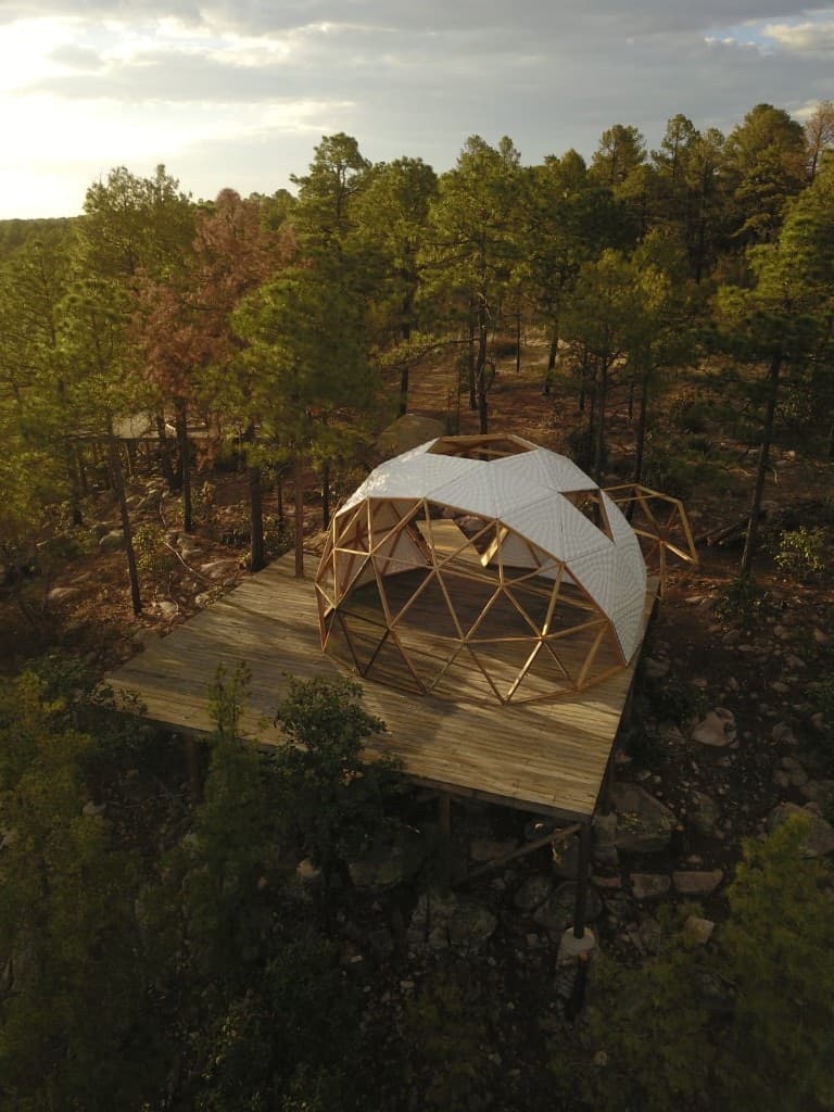Vista aérea del domo geodésico de El Edén sobre deck de madera entre pinos